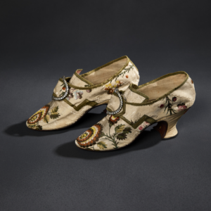 A pair of cream and floral-patterned silk heeled slippers with a metal and glass buckle.