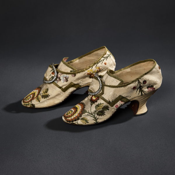 A pair of cream and floral-patterned silk heeled slippers with a metal and glass buckle.