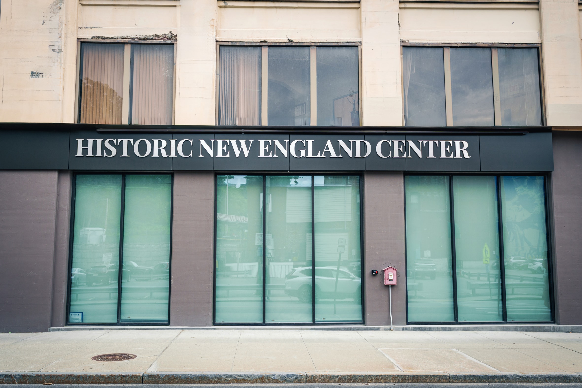 Exterior view of the first floor of a building with large lettering above three sets of glass doors reading Historic New England Center.