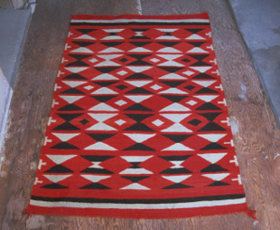 A woven red rug patterned with black and white diamonds and triangles laid on a wooden floor.
