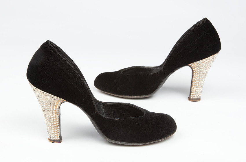 A pair of high-heeled black shoes with small studded white gems along the heels.