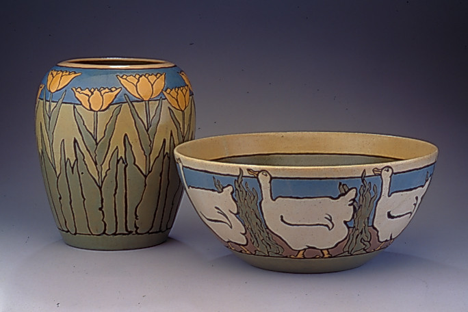 ID: A clay vase and bowl. The vase depicts orange tulips with green stems, leaves, and grass on a brown background with a blue sky, The bowl depicts white ducks with tall green grass between each duck on a brown background and blue sky.