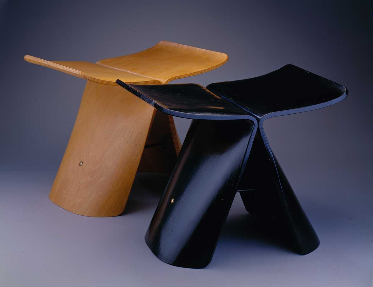 Two angular stools each made of two pieces of wood joined together just below the seat.