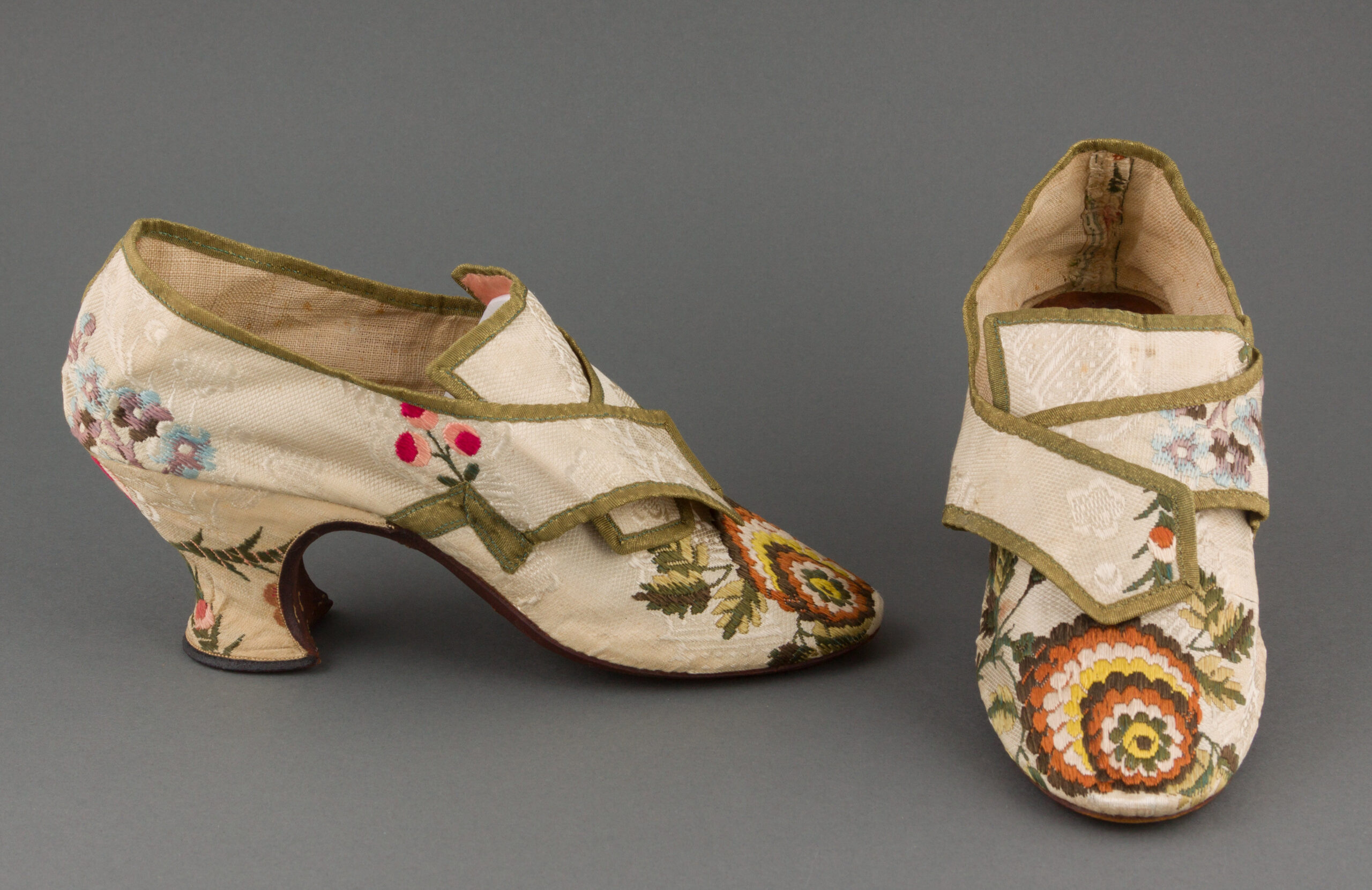 A pair of tan silk brocade shoes embroidered with floral patterns.